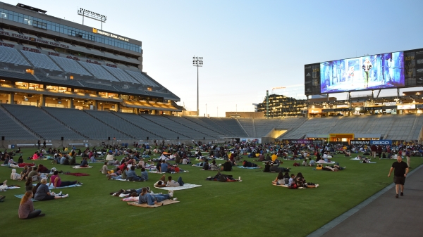 People lie on blankets on the football field in the ASU stadium as a movie plays on the screen