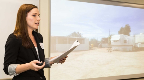 Woman in professional wear, Maggie Dellow, giving presentation with mobile home park depicted on slideshow