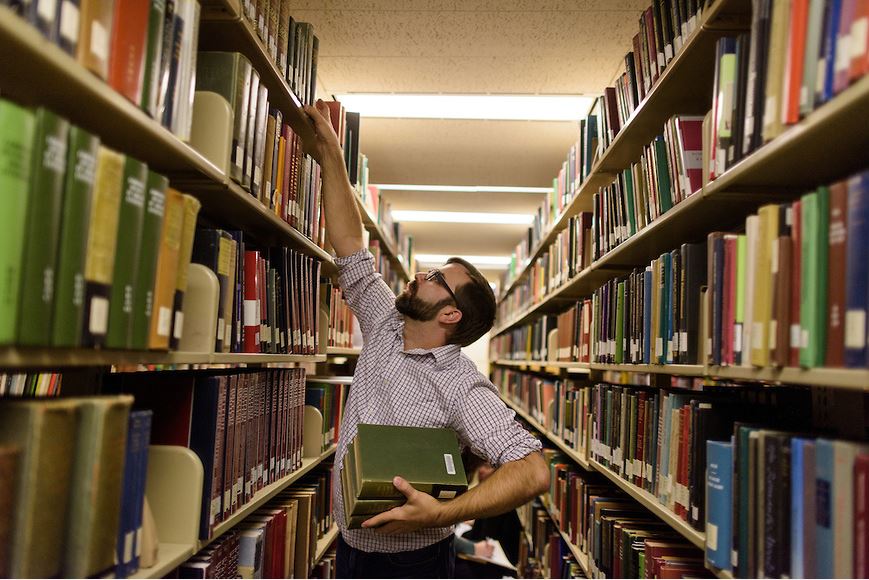 student reaching for book on library shelf