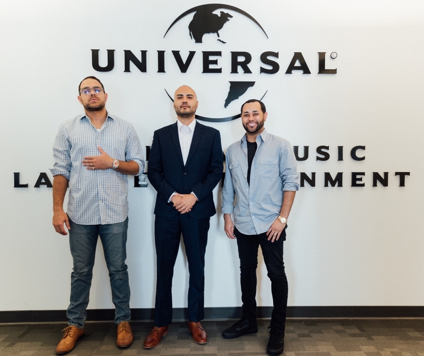 three men standing in front of Universal Music logo