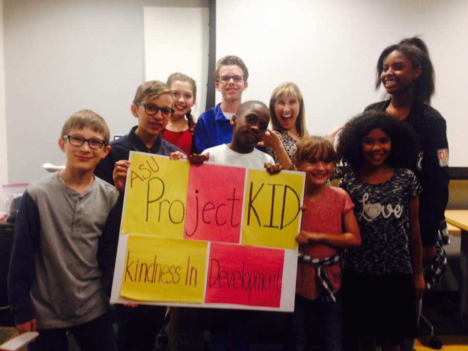 Picture of Tracy Spinrad and children holding a sign from Project Kid.