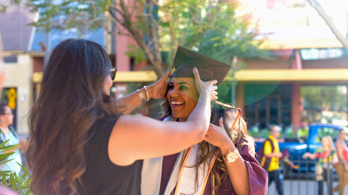 A graduate gets help adjusting her cap