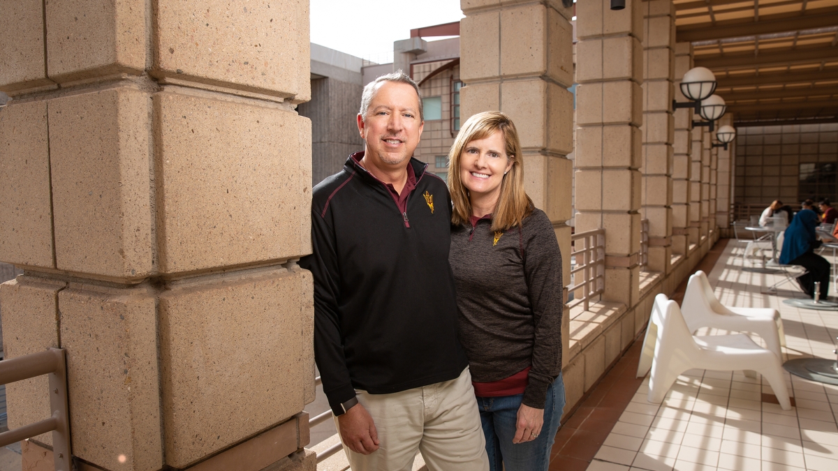 ASU alum husband and wife smiling in the hallway of a campus building