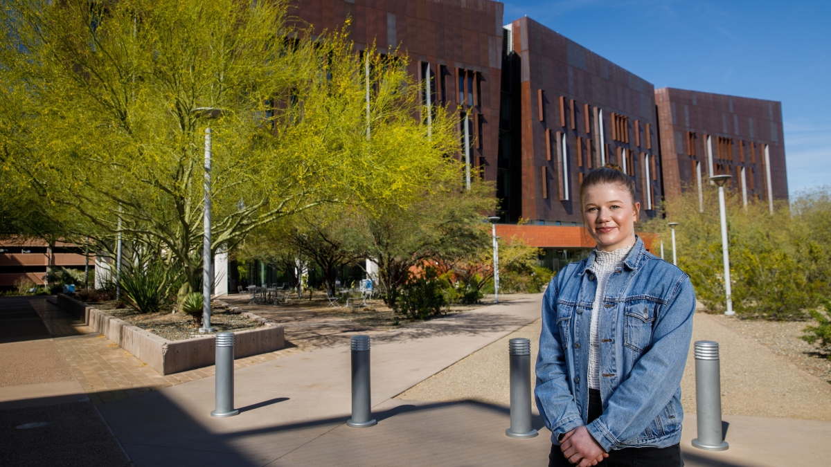 PhD exchange student Grace Colley stands outside a Biodesign building with desert landscaping