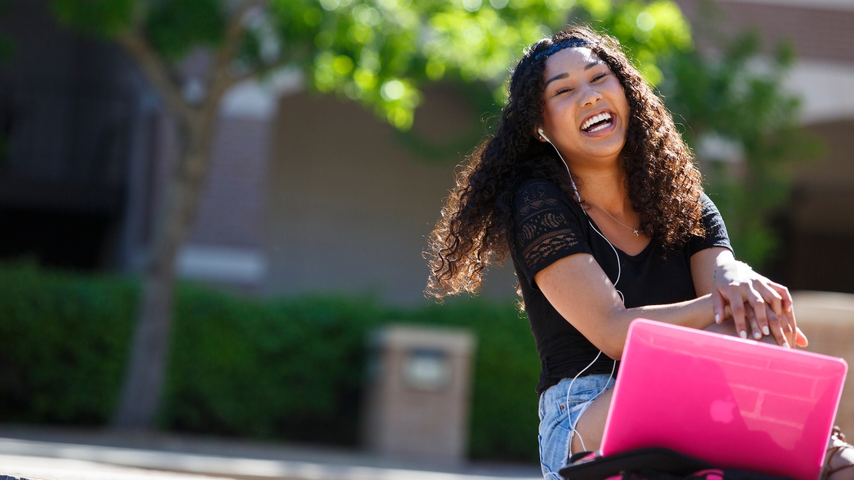 A student laughs as she sits outside with her laptop