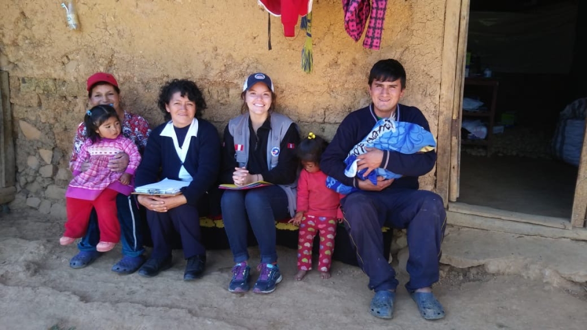 group of people sitting outside a mud brick home in Peru