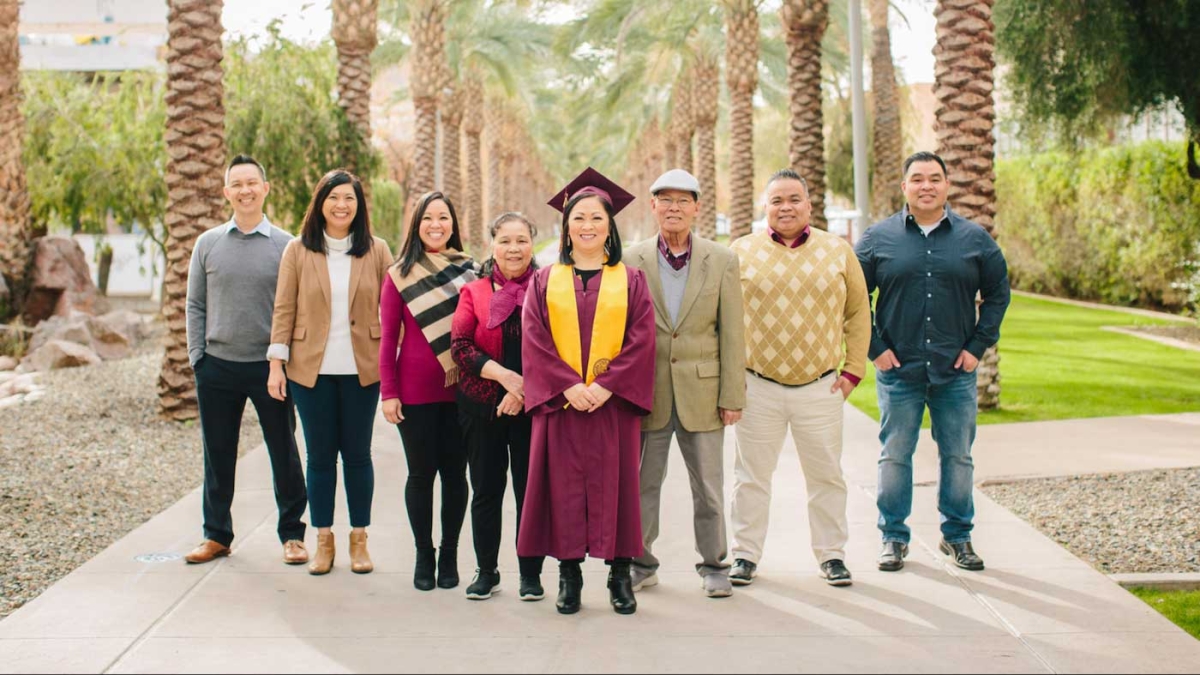 A woman in a cap and gown poses on Palm Walk with her family