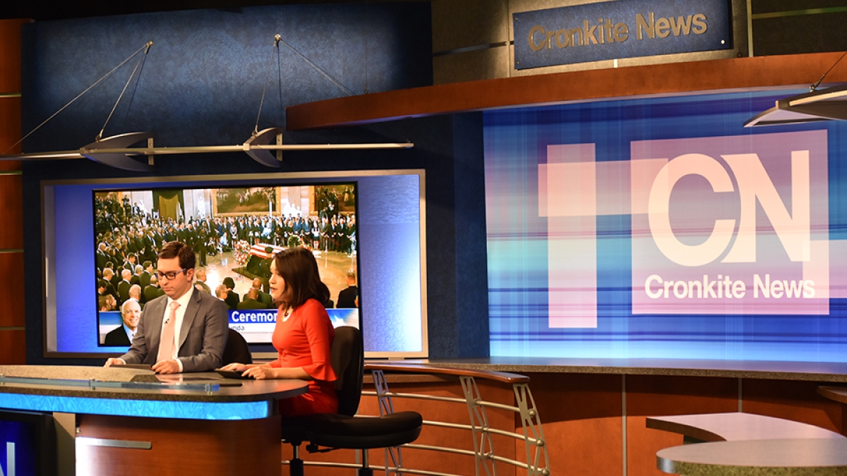 Journalists sit at a table in a TV broadcast studio