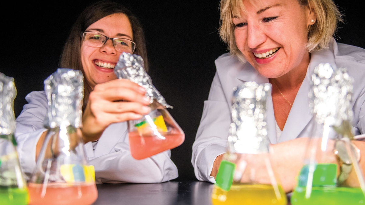 Two scientists examine beakers filled with different colored liquids