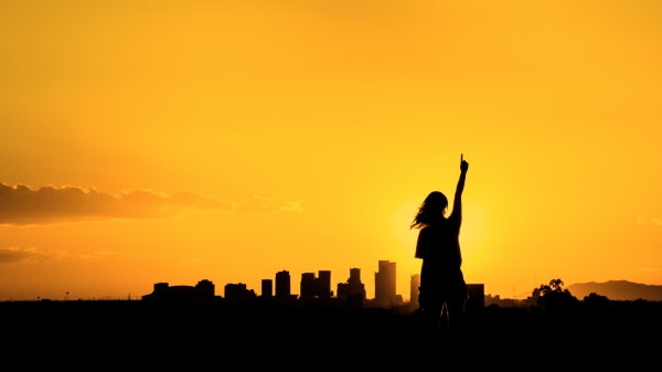 Silhouette of a woman pointing at the sky in front of the Phoenix skyline