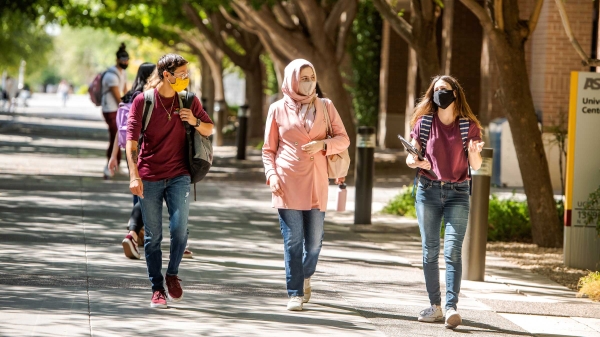 Three students wearing masks talk and laugh as they walk on campus