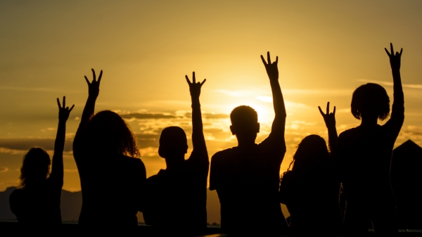 Group of people making ASU Pitchfork signs with their hands, silhouetted against a background of a setting sun.