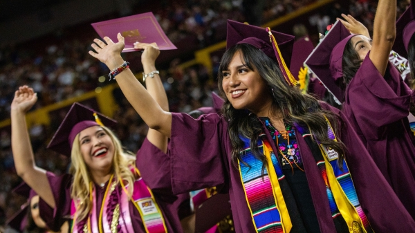 Women in graduation caps and gowns wave at their families