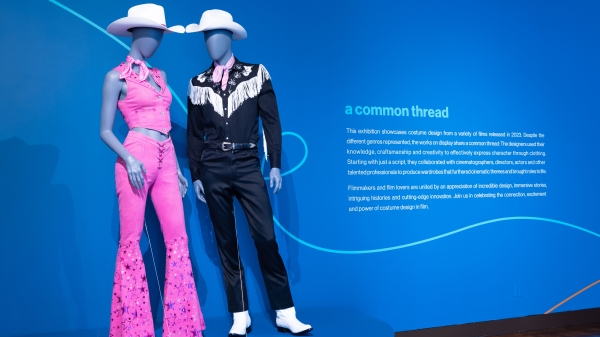 Costumes from the film "Barbie" — pink cowgirl and black cowboy outfits with white hats on mannequins — on display against a blue background at the ASU FIDM Museum in LA.
