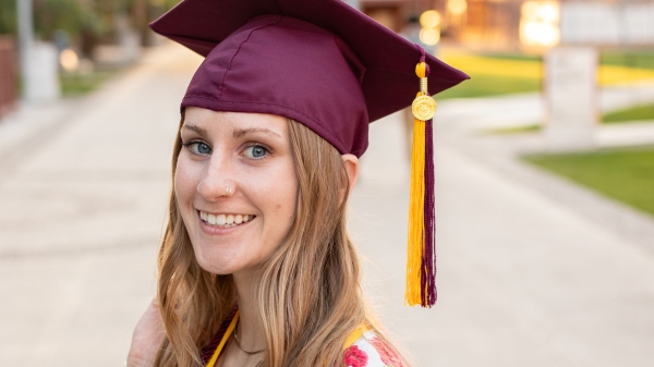 Kalyn Denton smiling at the camera in ASU Graduation regalia on the Tempe campus.