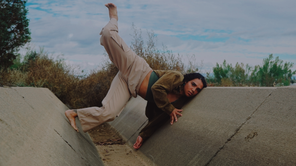 A dancer poses with leg extended against a concrete wall