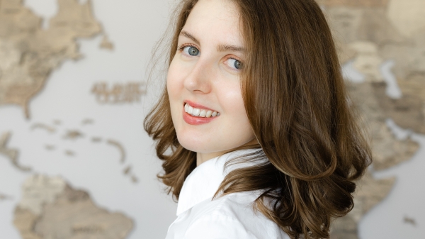 A brunette woman in a white blouse smiles for the camera. 