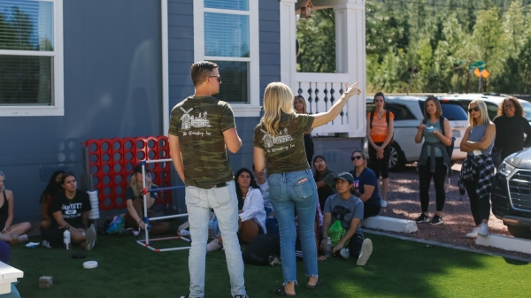 A group of students from ASU's Tourism Student Association listen to two people talk outside of a blue house with white trim.