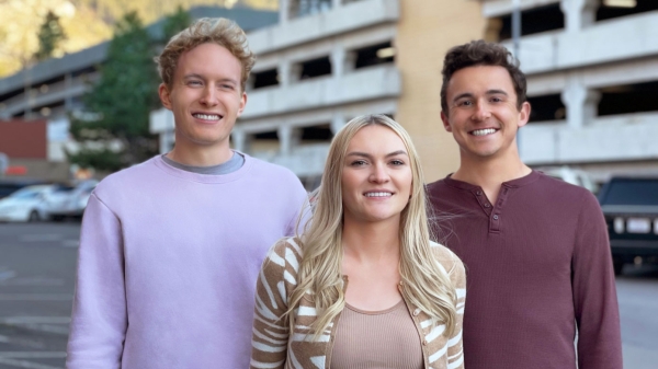 Two young men and a young woman pose in front of a parking garage