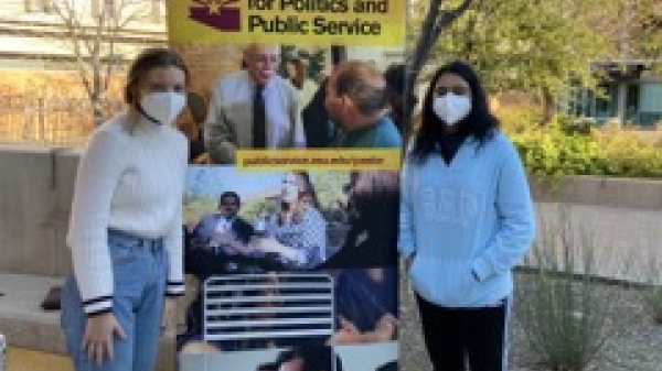 Two people wearing face coverings standing on either side of a banner that reads "Pastor Center for Politics and Public Service."