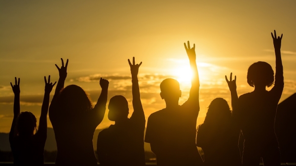 Silhouettes of six people giving the forks up hand signal in front of a sunset