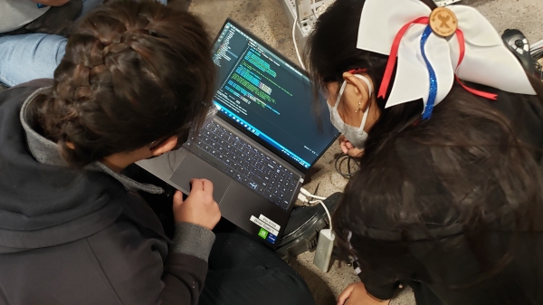 Students pictured from behind as they look at a laptop with coding on the screen.