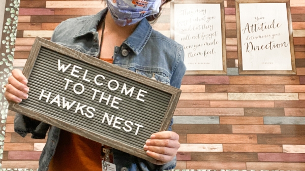 Lauren Hawks with a mask on and a sign that says Welcome to the Hawks nest