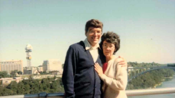 A man and a woman pose together on a bridge.