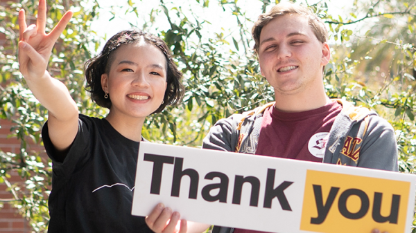 Two students hold a thank you sign and display a forks up hand gesture