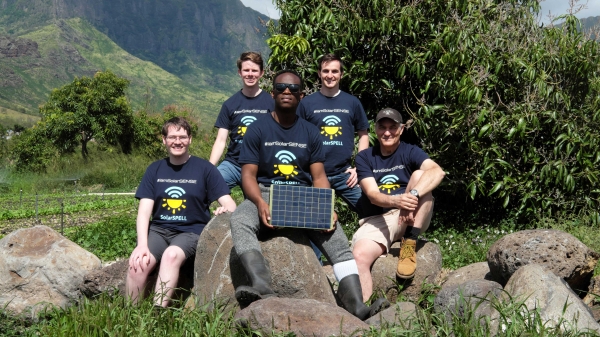 Five people sitting on rocks on farm in front of mountains with SolarSPELL unit