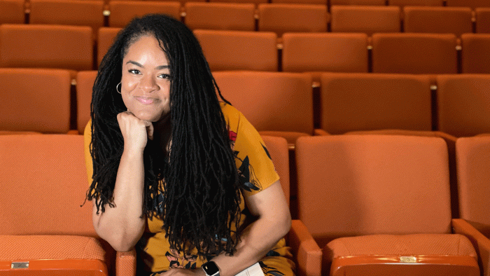 A woman leans on her hand smiling while sitting in theater seats