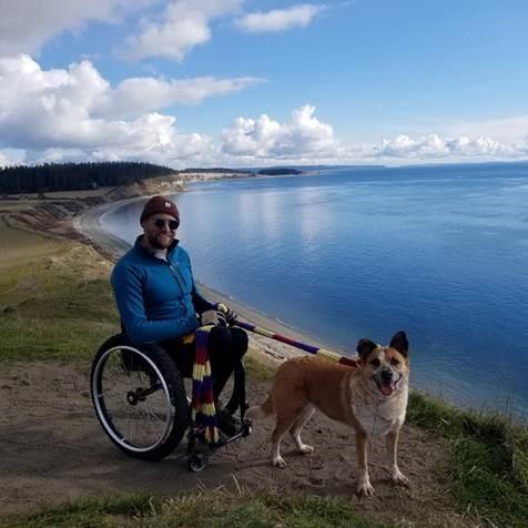 man in a wheelchair with a dog by a lake
